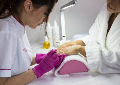 female beautician painting the nails of female customer in white bath robe