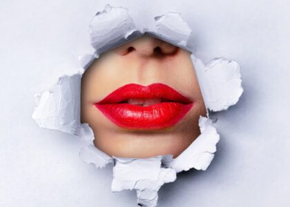 red lips peeking through a hole in a sheet of white paper