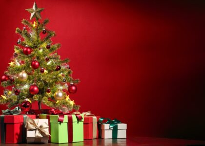 decorated christmas tree with presents underneath infront of a red wall